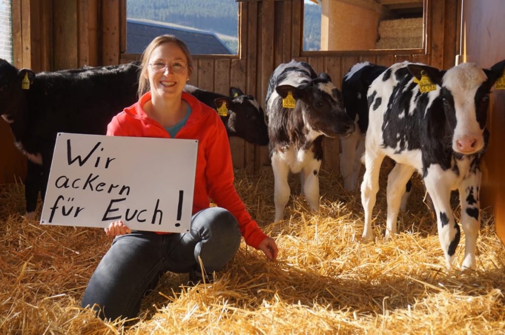 Frau in Kuhstall mit Plakat