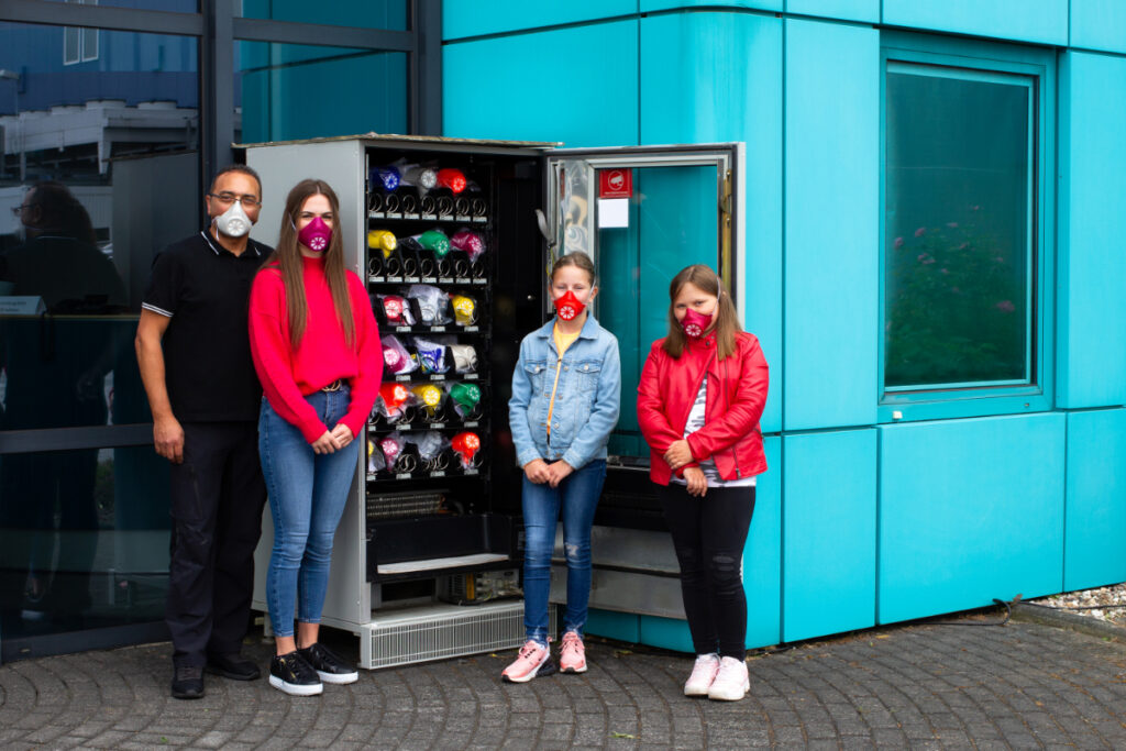 Vier Menschen vor Automat für Munschutzmasken