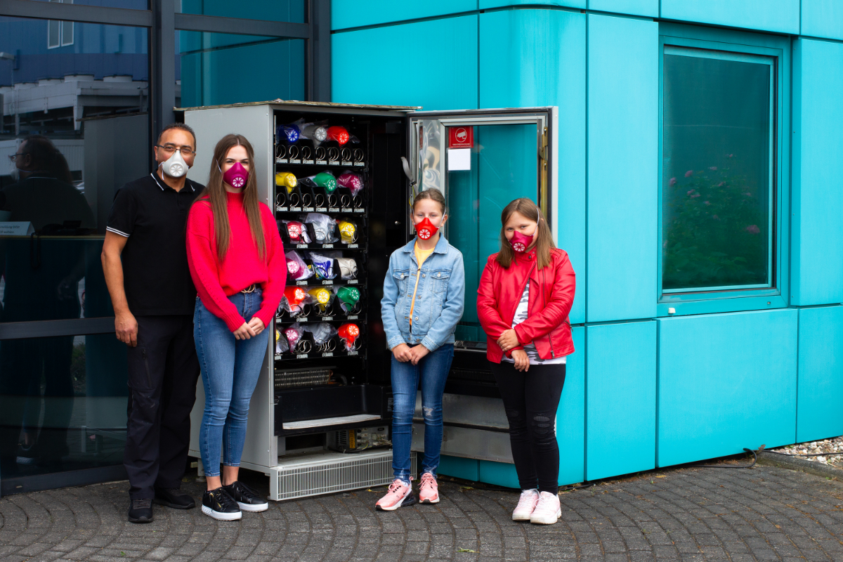 Vier Menschen vor Automat für Munschutzmasken