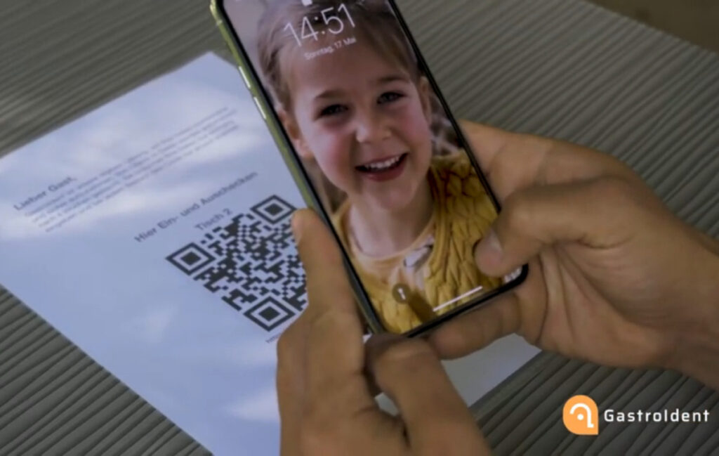 Handy mit Kinderbild, im Hintergrund Tisch mit QR-Code