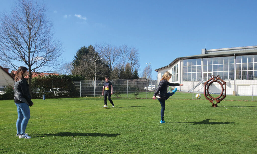 Jugendliche spielen mit Fußball auf Wiese