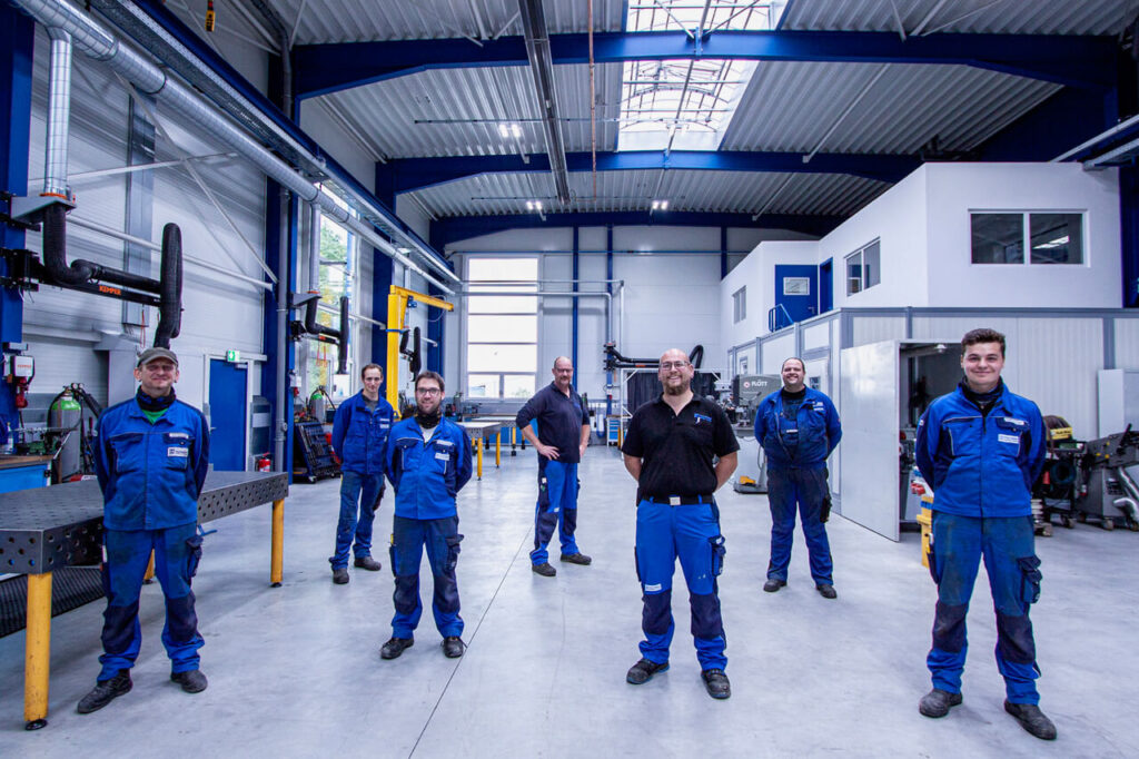 Männer in Arbeitskleidung stehen in einer Halle neben Maschinen