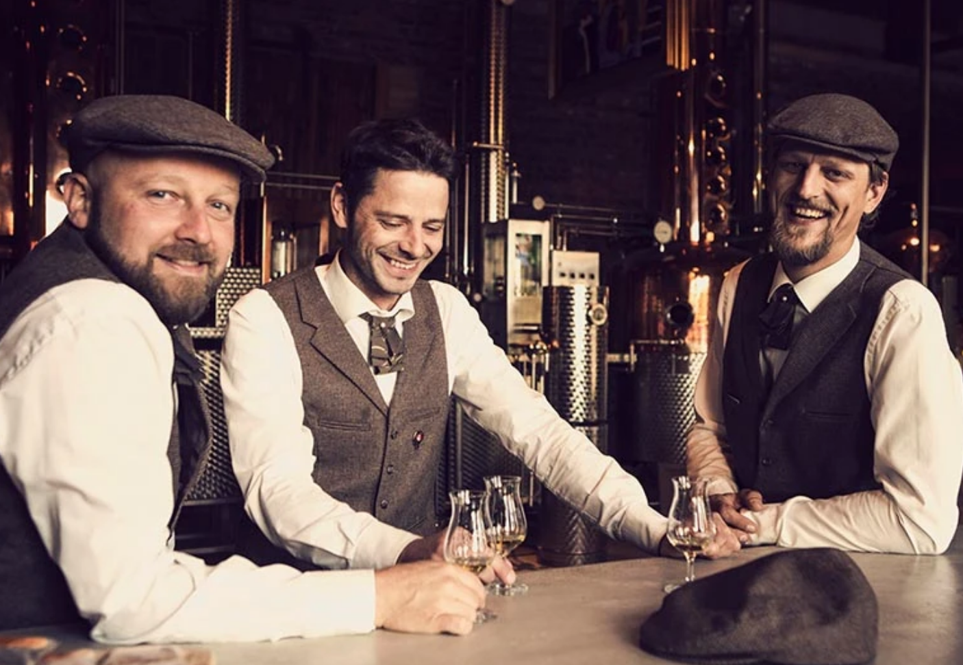 Drei Männer in Western-Style stehen mit Whisky an einer Theke