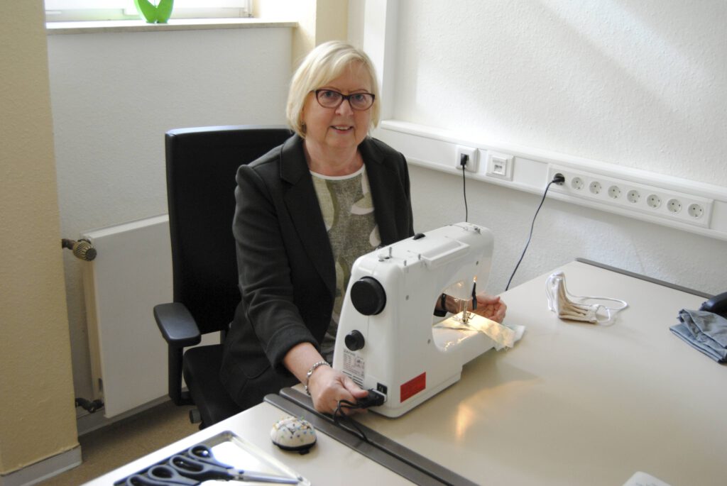 Frau sitzt an Tisch vor Nähmaschine