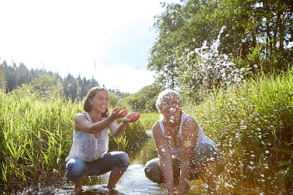Zwei Frauen knien in einem Bach und spritzen mit Wasser