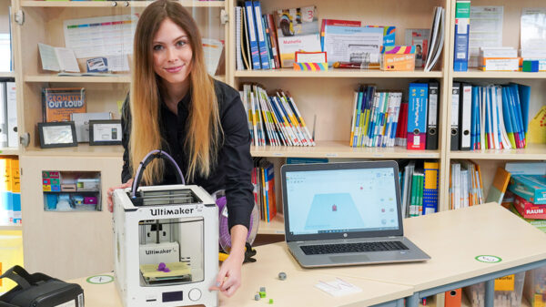 Frau steht hinter einem Tisch mit 3D-Drucker und Laptop