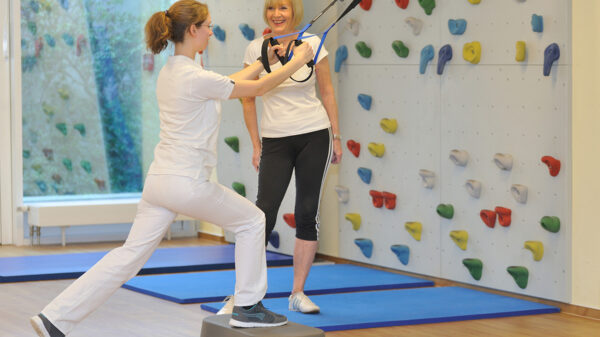 Frau im Vordergrund macht Sportübungen, eine zweite Frau hilft ihr.