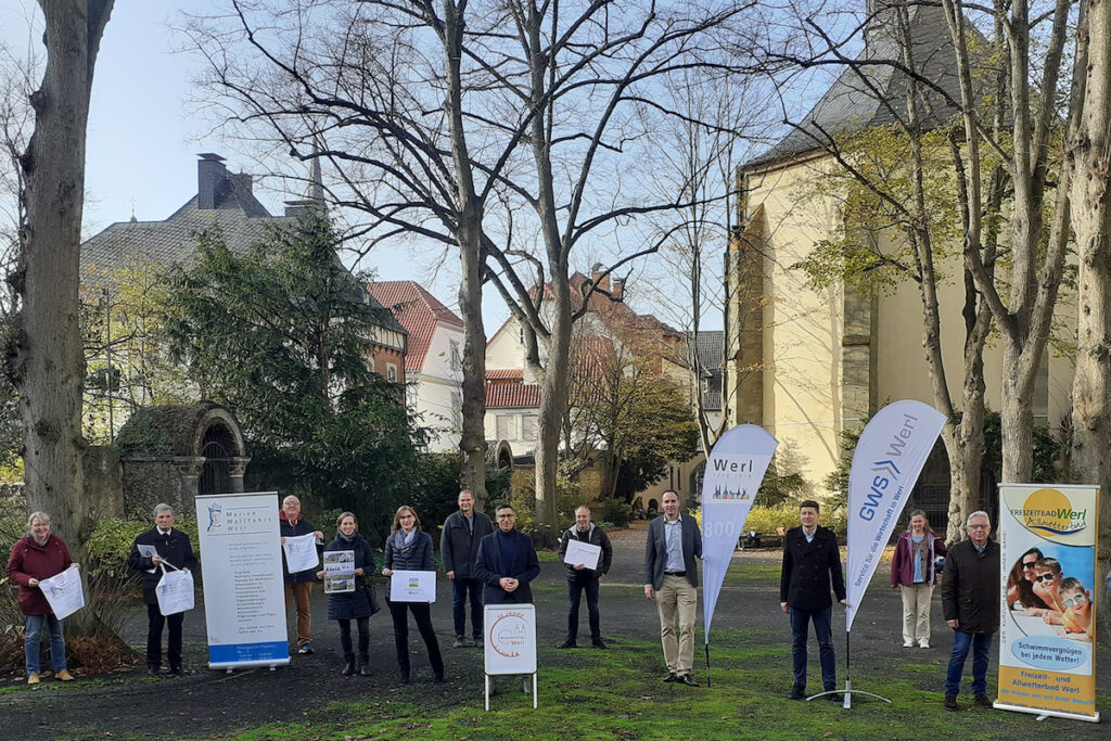 Zwölf Menschen stehen mit Plakaten nebeneinander auf einer Wiese