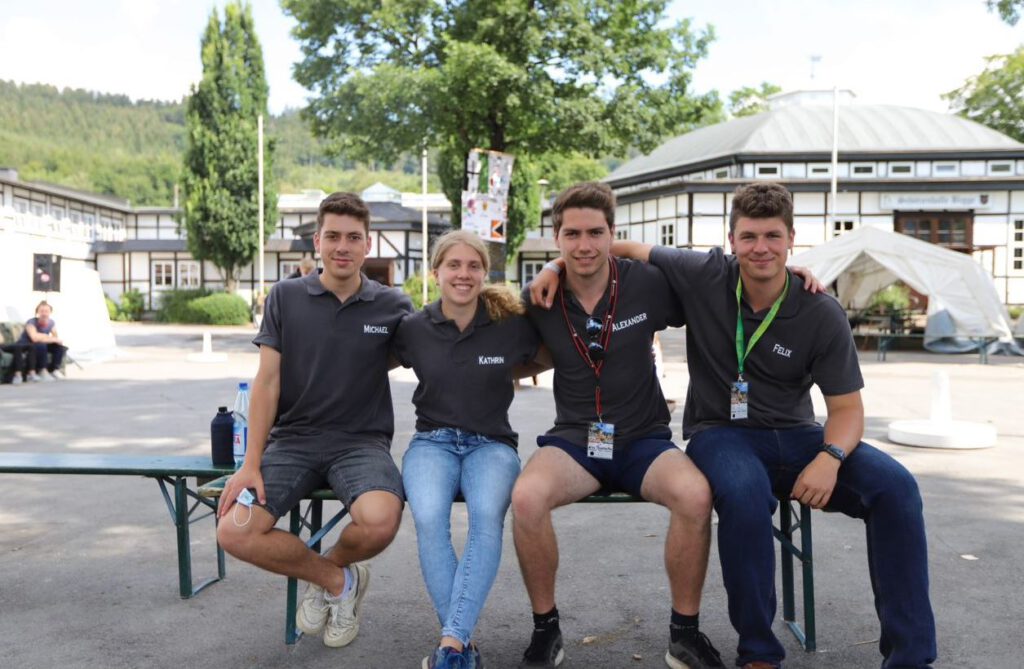 Vier junge Menschen sitzen auf einer Bank und schauen in die Kamera