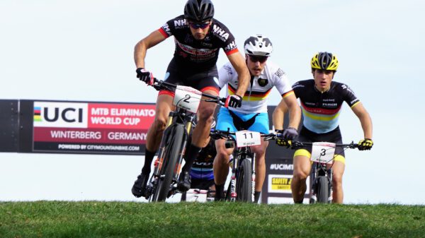 Drei Radfahrer in Sportkleidung fahren eng nebeneinander eine Wiese hinunter