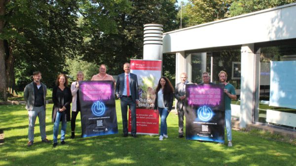 Neun Personen stehen auf einer Wiese und halten Plakate für die neue Kampagne in der Hand