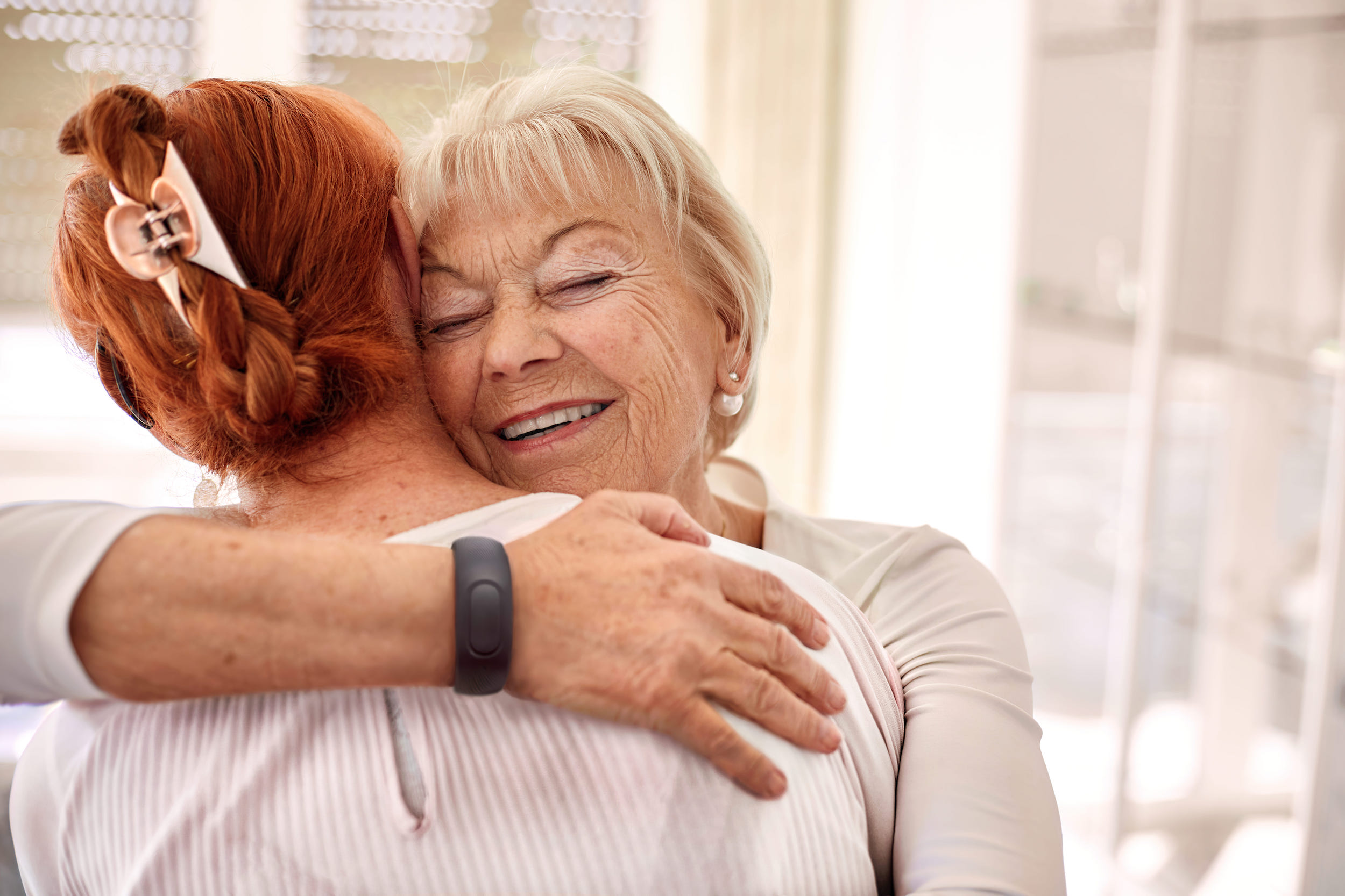 Eine ältere Dame umarmt eine andere Person. Am Handgelenk trägt sie ein Armband.
